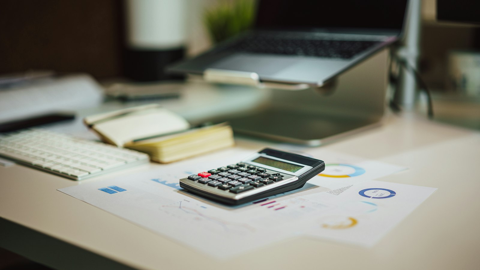 A calculator on a desk beside printed charts and a laptop