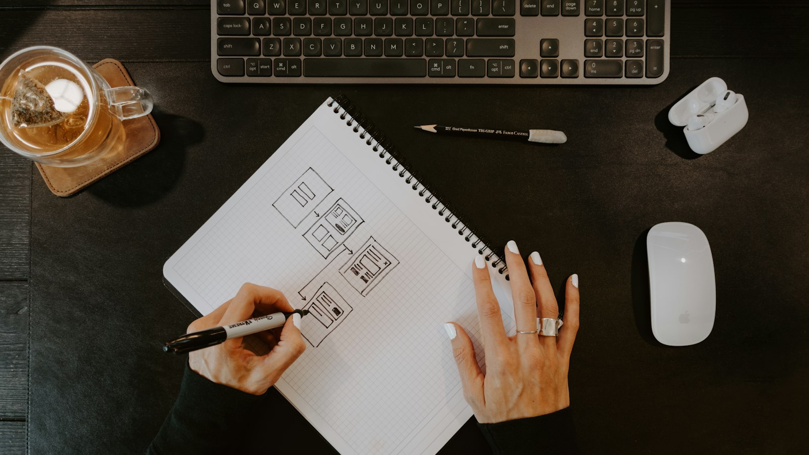 A designer sketching layouts in a notebook at a dark desk