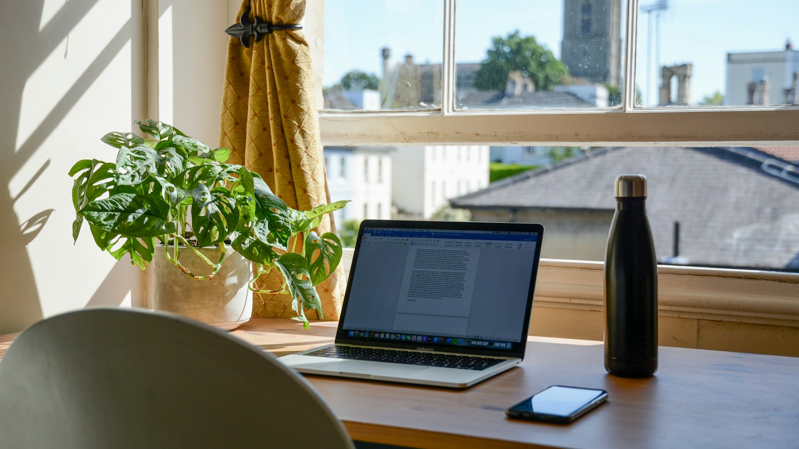A laptop on a desk by a sunny window with plants