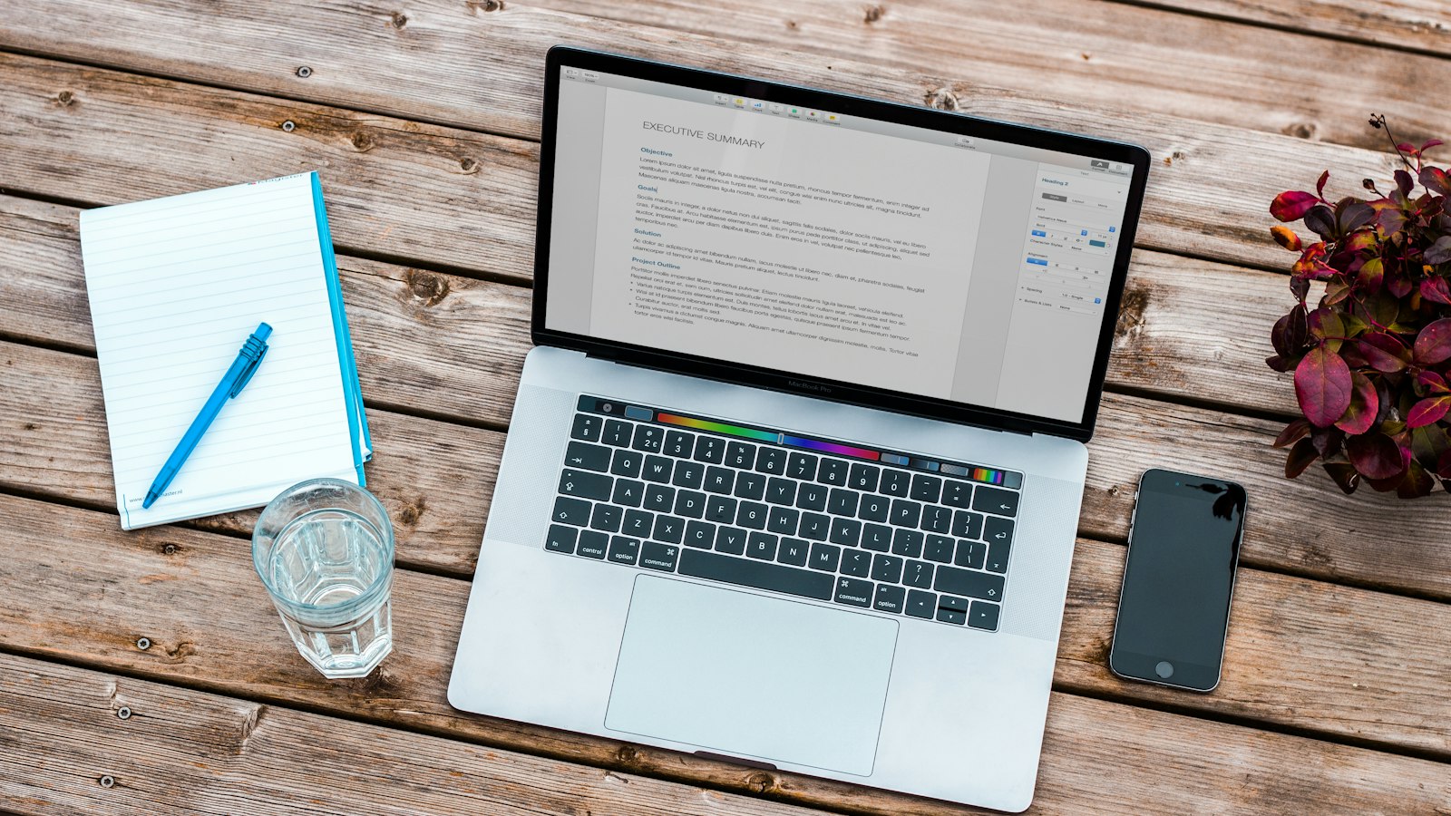 A laptop, notebook and phone on a wooden desk
