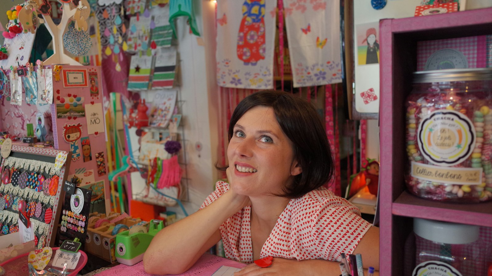 A small shop owner at her counter surrounded by colourful stock