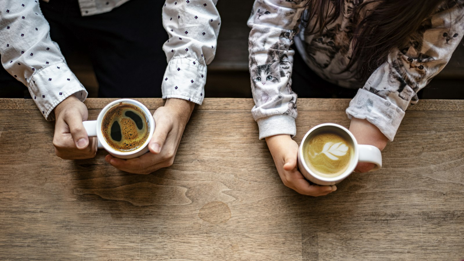Two people holding coffees across a wooden table