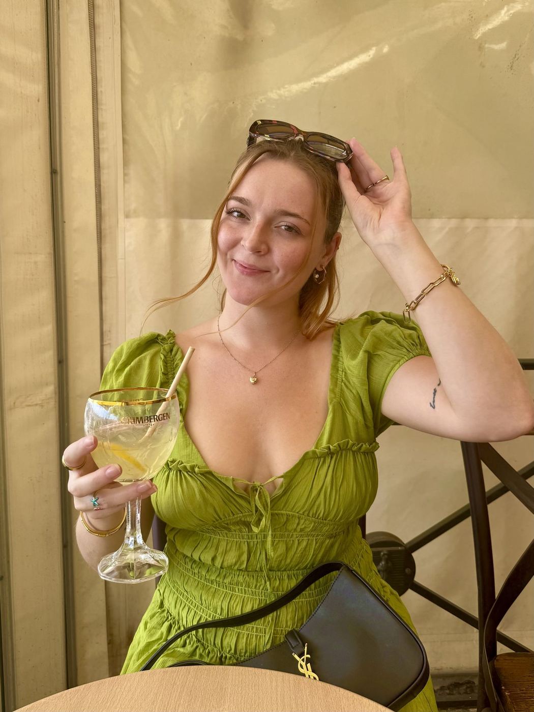 Indi in a green dress, drink in hand, saying hi