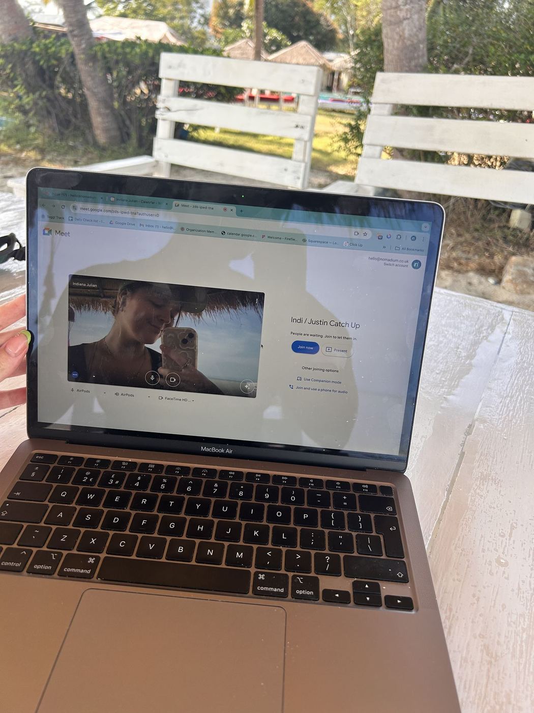 Indi on a client call, laptop propped on an outdoor table in the shade